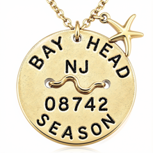 Load image into Gallery viewer, A gold-toned round Beach Tag pendant necklace engraved with 'BAY HEAD NJ 08742 SEASON' and a starfish charm, shown on a white background.