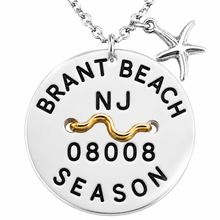 Load image into Gallery viewer, A silver round Beach Tag pendant necklace engraved with 'BRANT BEACH NJ 08008 SEASON' and a gold wave detail, featuring a silver starfish charm on a white background.