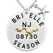 Load image into Gallery viewer, A silver round beach tag pendant necklace engraved with 'BRIELLE NJ 08730 SEASON' and a gold wavy accent, shown with a silver starfish charm on a white background.