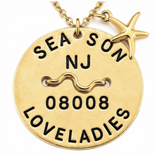 Load image into Gallery viewer, A gold-toned round Beach Tag pendant necklace engraved with 'SEA SON NJ 08008 LOVELADIES' and a wavy zodiac symbol, featuring a small starfish charm on a matching chain against a white background.