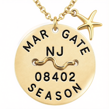 Load image into Gallery viewer, A gold-toned round beach tag pendant necklace engraved with 'MARGATE NJ 08402 SEASON' and a wavy line motif, shown with a small starfish charm on a white background.