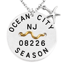 Load image into Gallery viewer, A silver-toned round beach tag pendant necklace with a starfish charm, featuring the text 'OCEAN CITY NJ 08226 SEASON' and a wavy gold accent on a white background.