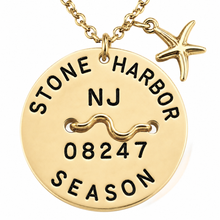 Load image into Gallery viewer, A gold-toned round beach tagpendant necklace engraved with 'STONE HARBOR NJ 08247 SEASON' and a wavy line motif, shown with a starfish charm on a white background.