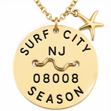 Load image into Gallery viewer, A gold-toned round beach tag pendant necklace with a starfish charm, featuring the text 'SURF CITY NJ', a wave symbol, '08008', and 'SEASON' engraved on a clean white background.