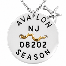 Load image into Gallery viewer, A silver round beach tag pendant necklace with a starfish charm, featuring black engraved text reading 'AVA LON NJ 08202 SEASON' and a wavy gold accent, shown on a white background.
