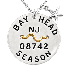 Load image into Gallery viewer, A silvertone round beach tag pendant necklace engraved with 'BAY HEAD NJ 08742 SEASON' and a gold wave detail, featuring a small silver starfish charm on a white background.
