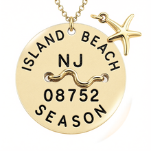 Load image into Gallery viewer, A gold-toned round beach tag pendant necklace engraved with 'ISLAND BEACH', 'NJ', '08752', and 'SEASON', featuring a wavy bar over the middle and a small starfish charm, shown on a white background.
