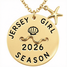 Load image into Gallery viewer, A gold-toned round beach tag pendant necklace with a starfish charm, featuring the engraved text 'JERSEY GIRL 2026 SEASON' and a seashell motif on a white background.
