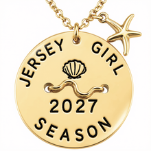 Load image into Gallery viewer, A gold-toned round beach tag pendant necklace engraved with 'JERSEY GIRL 2027 SEASON' and a seashell motif, with a small starfish charm on a matching chain against a white background.
