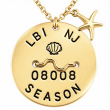Load image into Gallery viewer, A gold-toned round beach tag pendant necklace with a starfish charm, featuring engraved black text reading 'LBI NJ', a seashell motif, a wavy line, '08008', and 'SEASON'.
