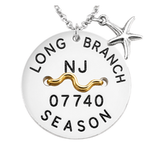 Load image into Gallery viewer, A silver-toned round beach tag pendant necklace with a starfish charm, featuring engraved text reading 'LONG BRANCH NJ 07740 SEASON' and a gold wavy accent bar across the center, shown on a white background.
