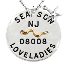 Load image into Gallery viewer, A silver round Beach Tag pendant necklace engraved with 'SEA &amp; SON', 'NJ', '08008', and 'LOVELADIES', featuring a gold wavy accent and a silver starfish charm, shown on a white background.
