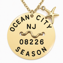 Load image into Gallery viewer, A gold-toned round beach tag pendant necklace engraved with 'OCEAN CITY NJ 08226 SEASON' and a wavy line, featuring a small starfish charm, on a white background.
