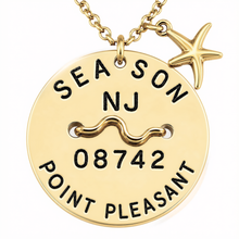 Load image into Gallery viewer, A gold-toned round beach tagpendant necklace with a starfish charm, featuring engraved text reading 'SEA SON NJ 08742 POINT PLEASANT' and a wavy line motif, shown on a white background.
