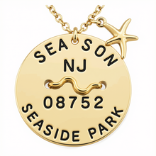 Load image into Gallery viewer, A gold round beach tag pendant necklace engraved with 'SEASON NJ 08752 SEASIDE PARK' and a wavy line, featuring a small gold starfish charm on a white background.
