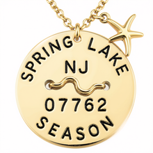 Load image into Gallery viewer, A gold-toned round beach tag pendant necklace engraved with 'SPRING LAKE NJ 07762 SEASON' and a wavy line symbol, featuring a small starfish charm on a white background.
