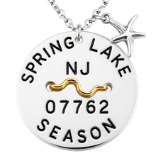 Load image into Gallery viewer, A silver round beach tag pendant necklace engraved with 'SPRING LAKE NJ 07762 SEASON' and a wavy gold accent, featuring a silver starfish charm on a white background.
