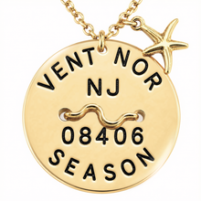 Load image into Gallery viewer, A gold-toned round beach tag pendant necklace with a starfish charm, featuring the engraved text 'VENT NOR NJ 08406 SEASON' and a wavy line symbol, shown on a white background.
