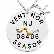 Load image into Gallery viewer, A silver round beach tag pendant necklace with black engraved text reading 'VENT NOR NJ 08406 SEASON' and a small gold wavy bar, plus a silver starfish charm, shown on a white background.
